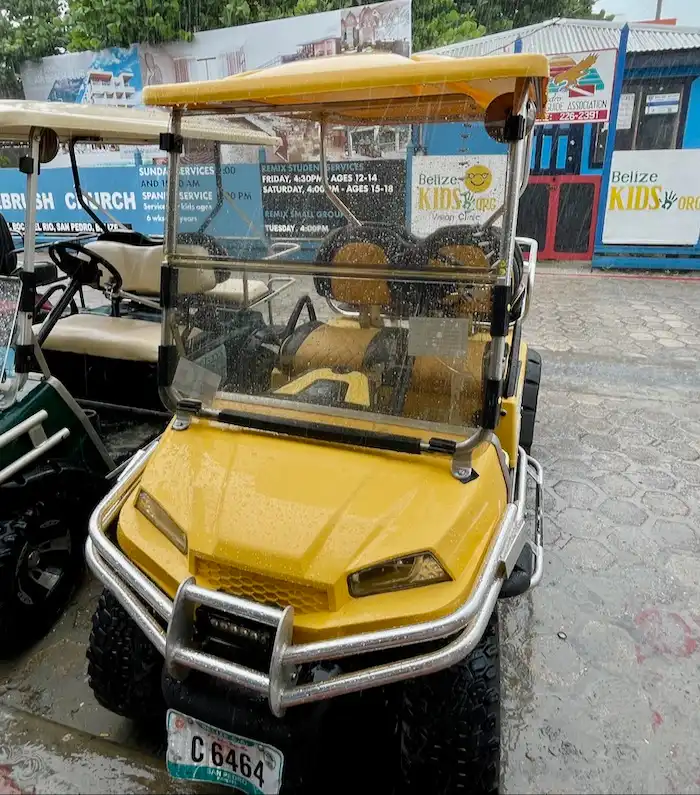 An empty yellow golf cart, slightly wet from the rain.