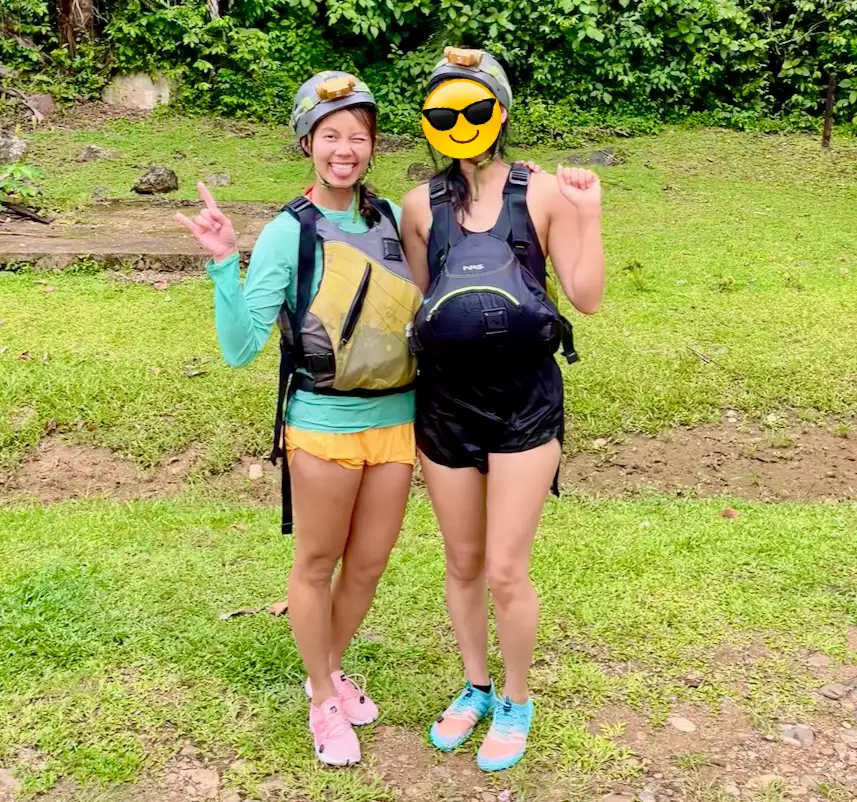 Two women wearing helmets, life vest, water shoes and shorts, while slightly wet.