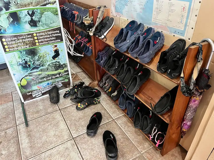Over a dozen worn shoes and water shoes on a shelf.