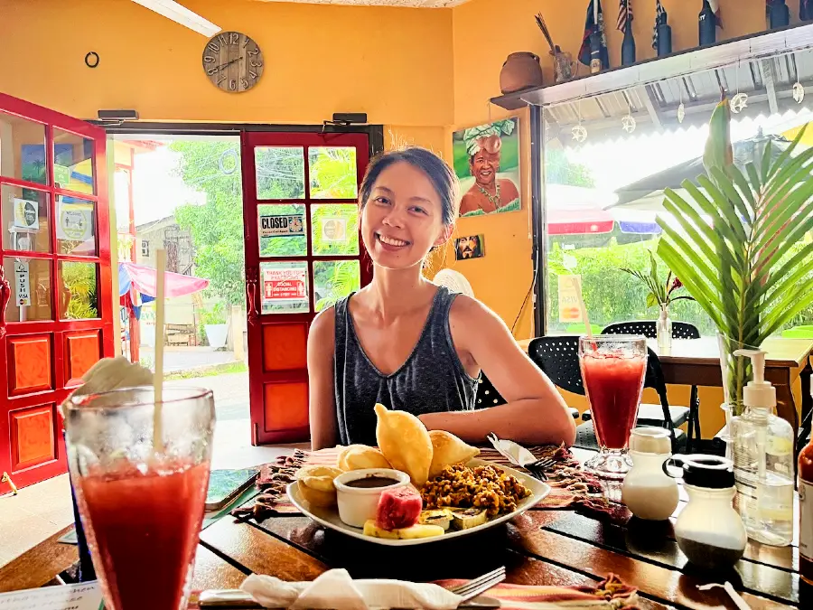 The blog author smiling in a restaurant with a a plate of watermelon, beans and puffy pastries.