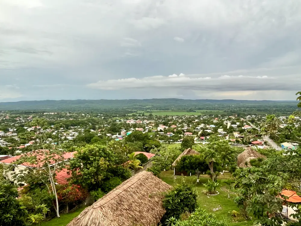 View from the top of a tropical, tree-filled town with a cloudy and rainy sky.