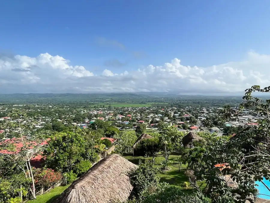 View from high-up of a tropical, green town with blue sky and some clouds.