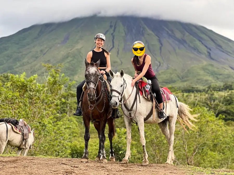 Two people riding horses with a covered volcano in the background.