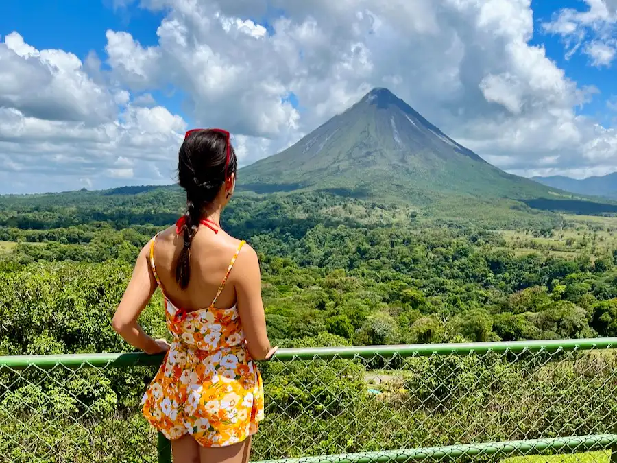 The blog author looking out at a lush green rainforest with a volcano in the background.