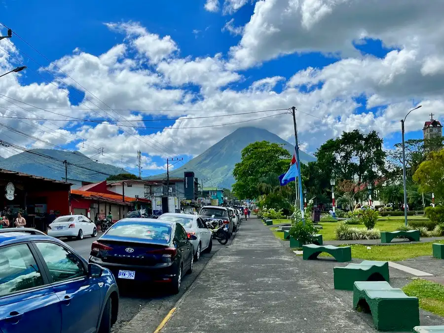 A small town sidewalk with a volcano in the background.