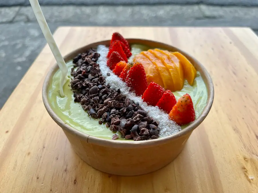 A bowl of acai-like smoothie topped with cocoa leaves, strawberries and mango.