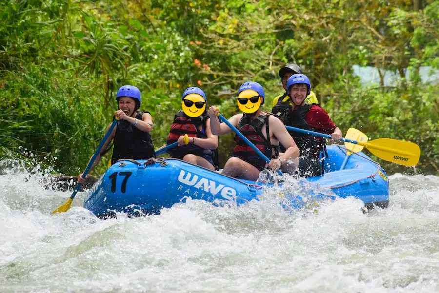 Four tourists on a raft paddling through rough whitewater river.