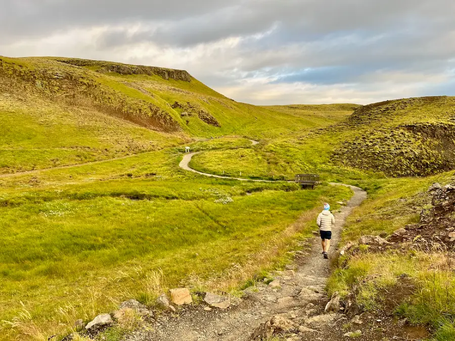 A man walking on a trail surrounded by green valley.