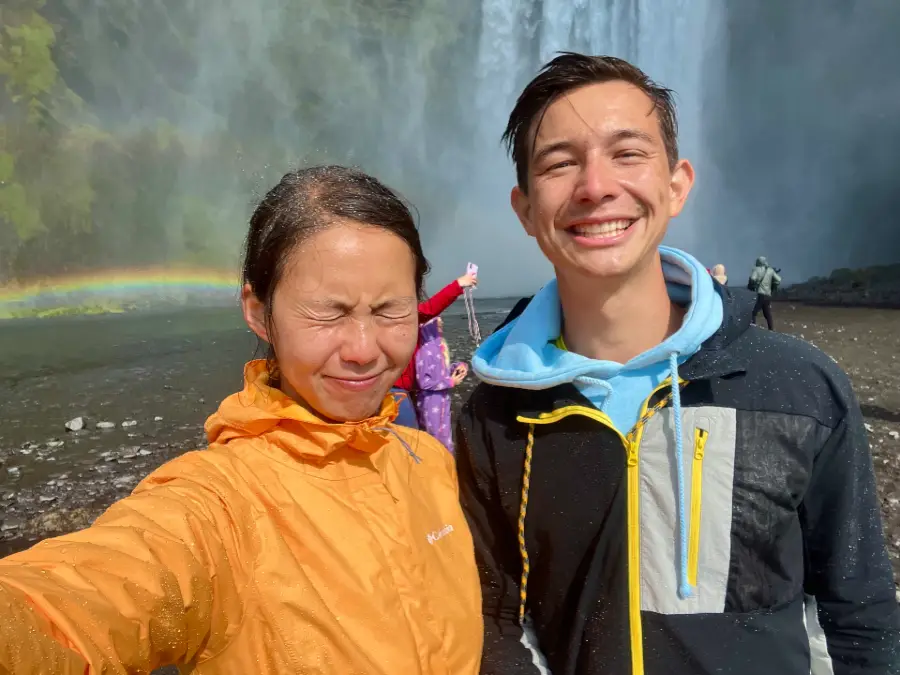A selfie of a woman with her eyes closed from getting wet. A man, who is also wet, stands beside her.