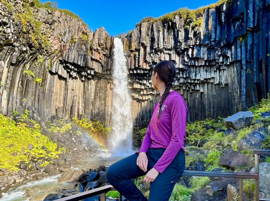 Blog author looking at a waterfall flowing between basalt columns.