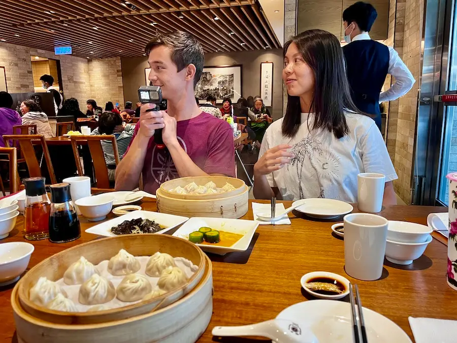 Two people sitting at a dining table with dozen of soup dumplings in front of them.