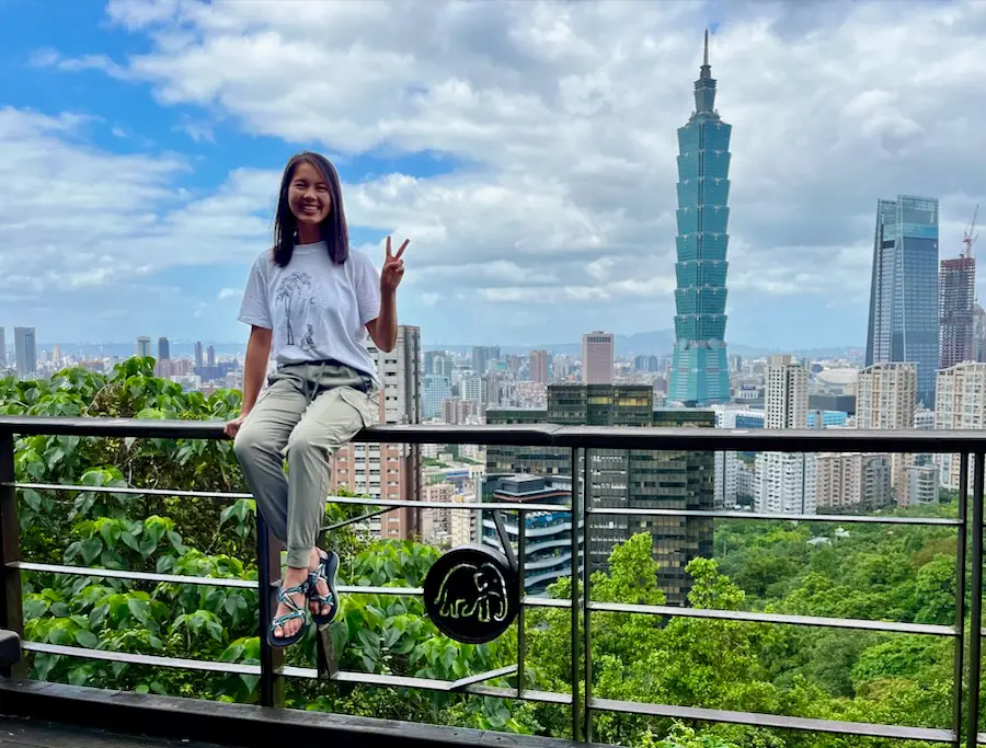 A woman sitting on a railing with an elephant symbol and a tall building in the background.