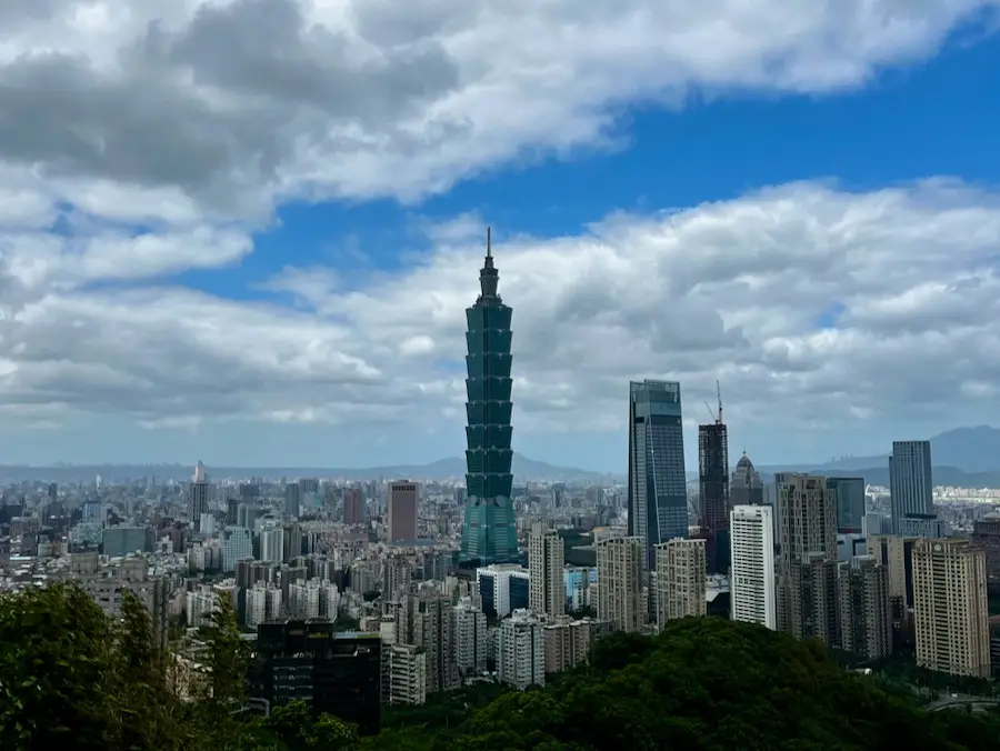 A tall, teal building towering Taipei's city skyline against a blue sky.