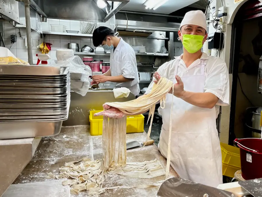 A chef with a mask proudly holding out fresh, handmade noodles.