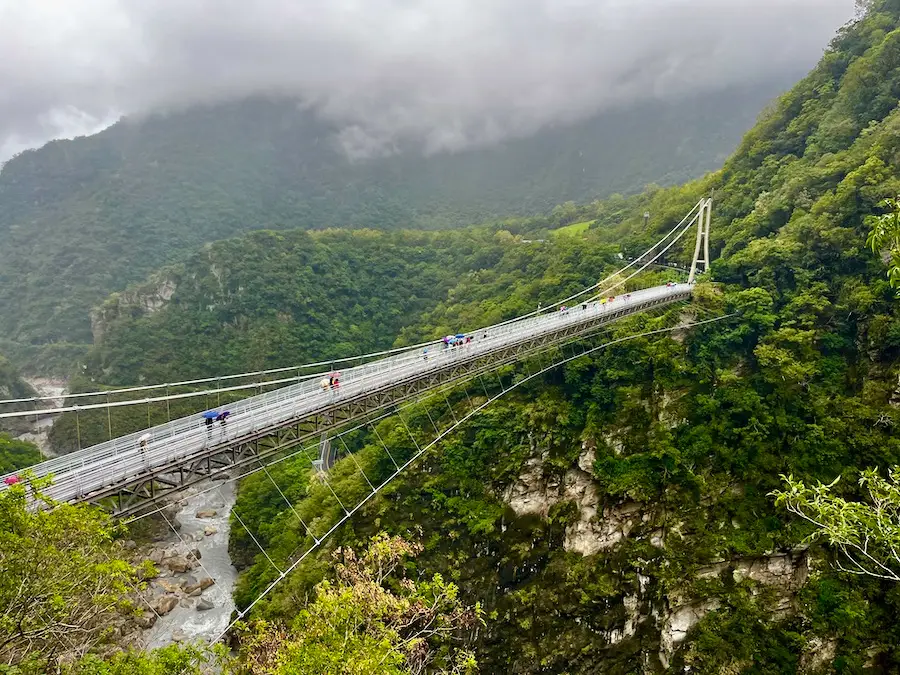 A long suspension bridge on a mountain with green trees.