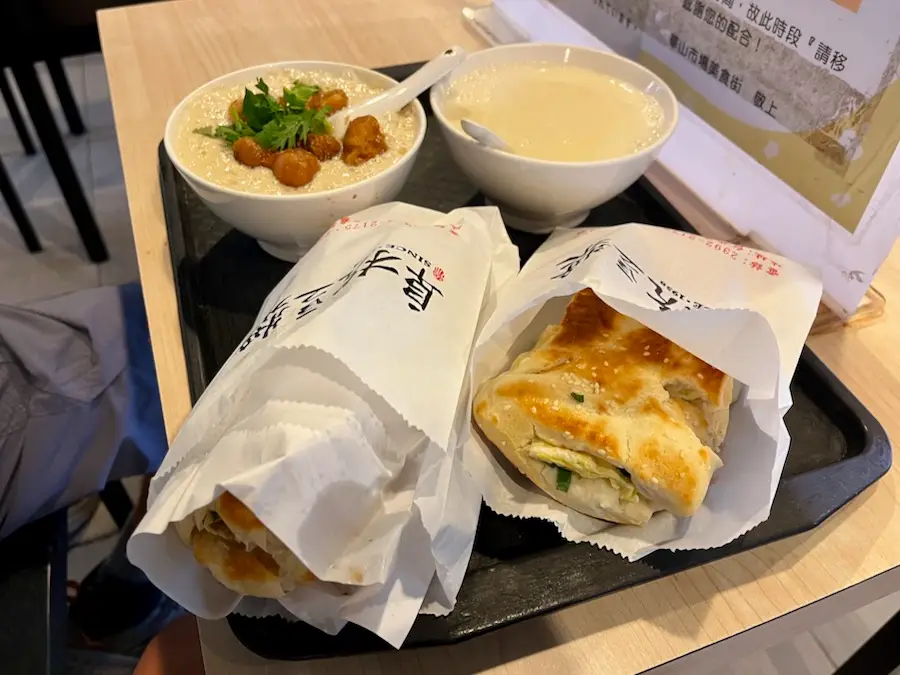 Two bread sandwiches with eggs and two soy milk in bowls, one which has fried bread dough.