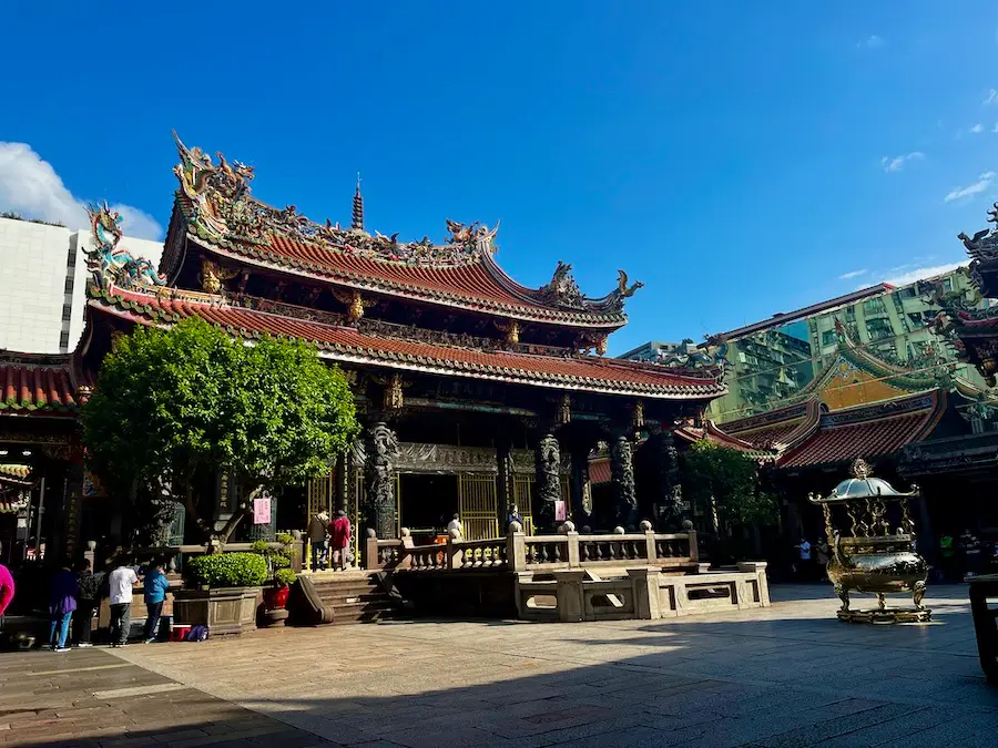 An Asian-style temple with decorative dragon roofs and people praying around it.