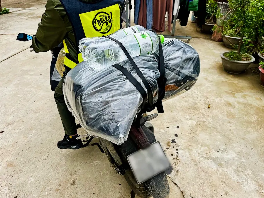A packback inside a clear plastic bag tied to the back of a motorbike.