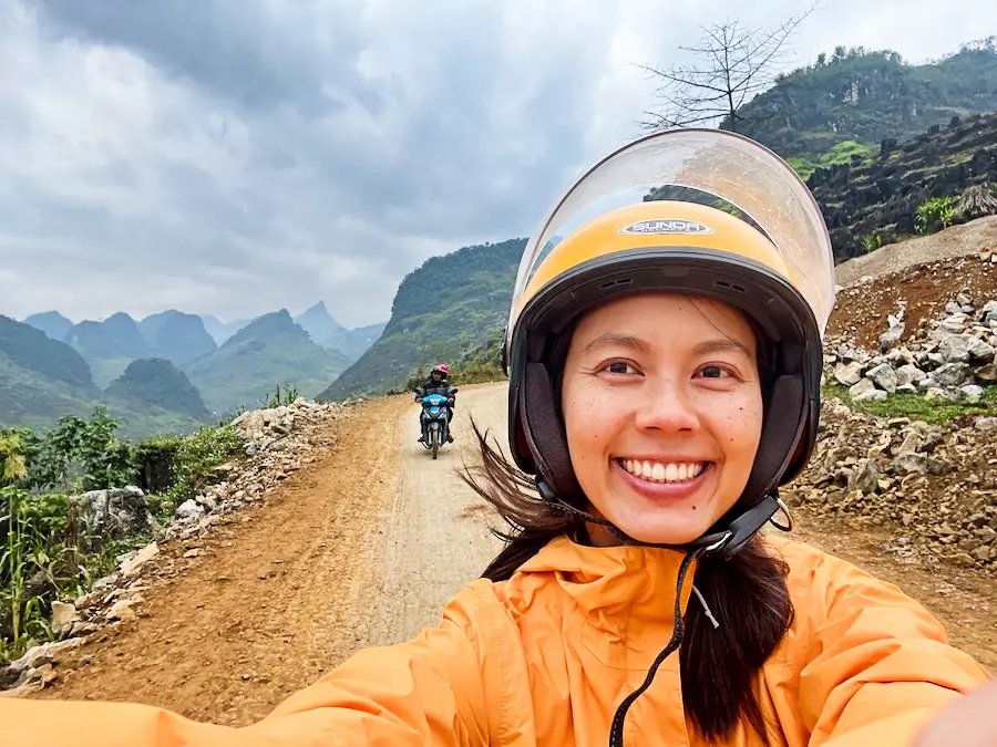 The blog author taking a selfie with a helmet while riding a motorbike through mountains.