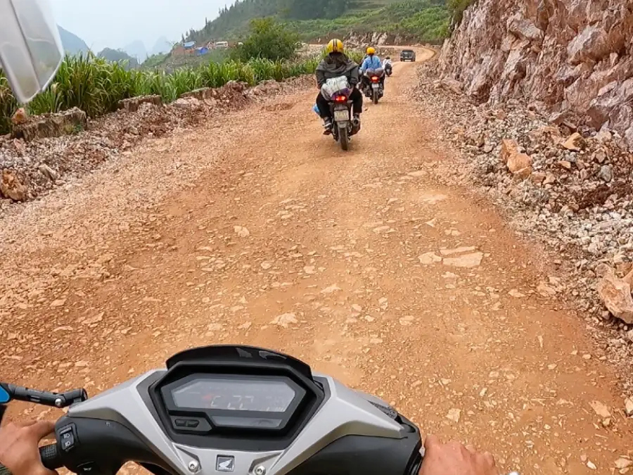 A non-paved, dirt road with motorbikes driving on it.
