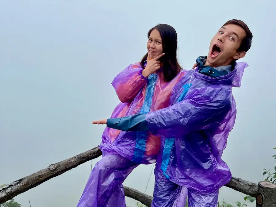 Two people wearing full-body ponchos and pointing at a completely foggy view where you cannot see anything.