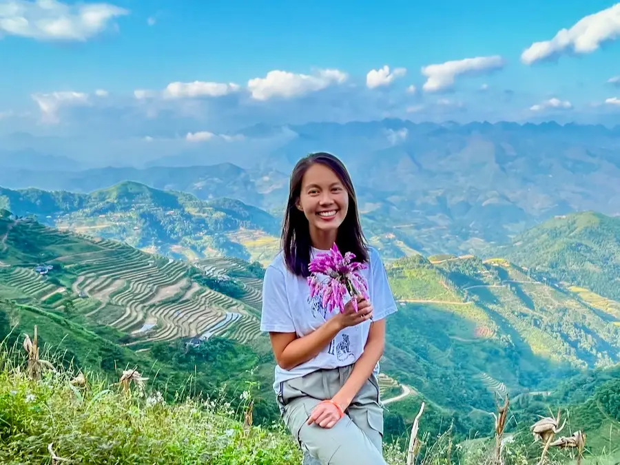 The blog author holding a flower with mountain views in the background.