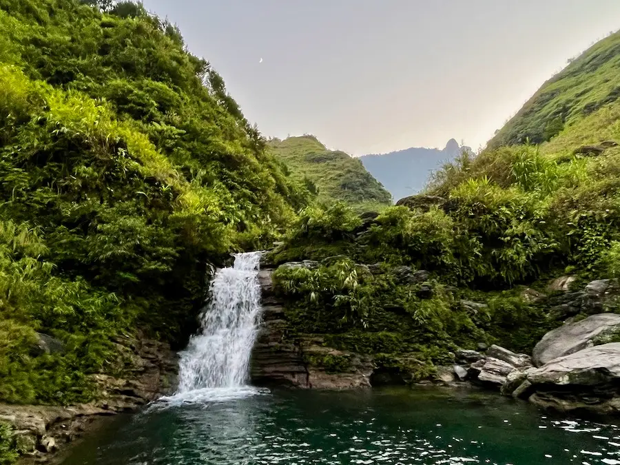 A small waterfall falling out of a small green mountain.