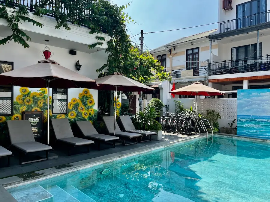 A clear pool with a row of sun chairs and umbrella.