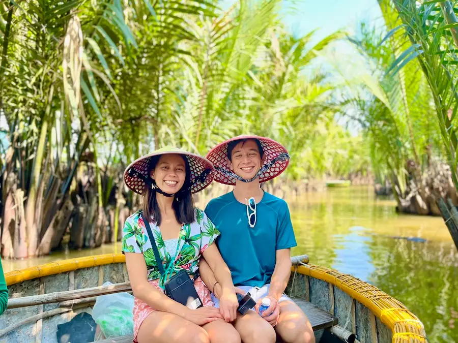 A couple with Vietnamese straw hats sitting on a bowl-shaped boat.