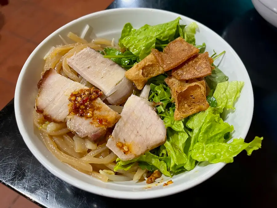 A noodle dish with yellow-tinted noodles, pork and vegetables.