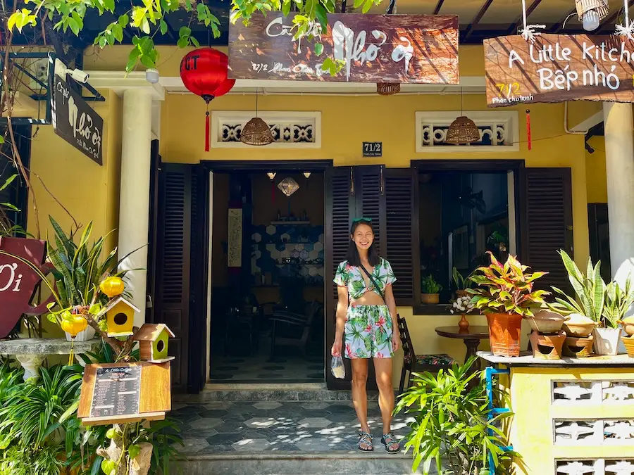 The blog author standing in front of a coffee shop with many plants.