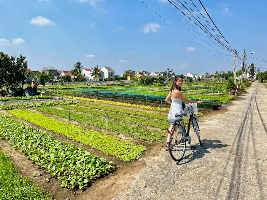 The blog's author holding a bike next to a field of farm vegetables.