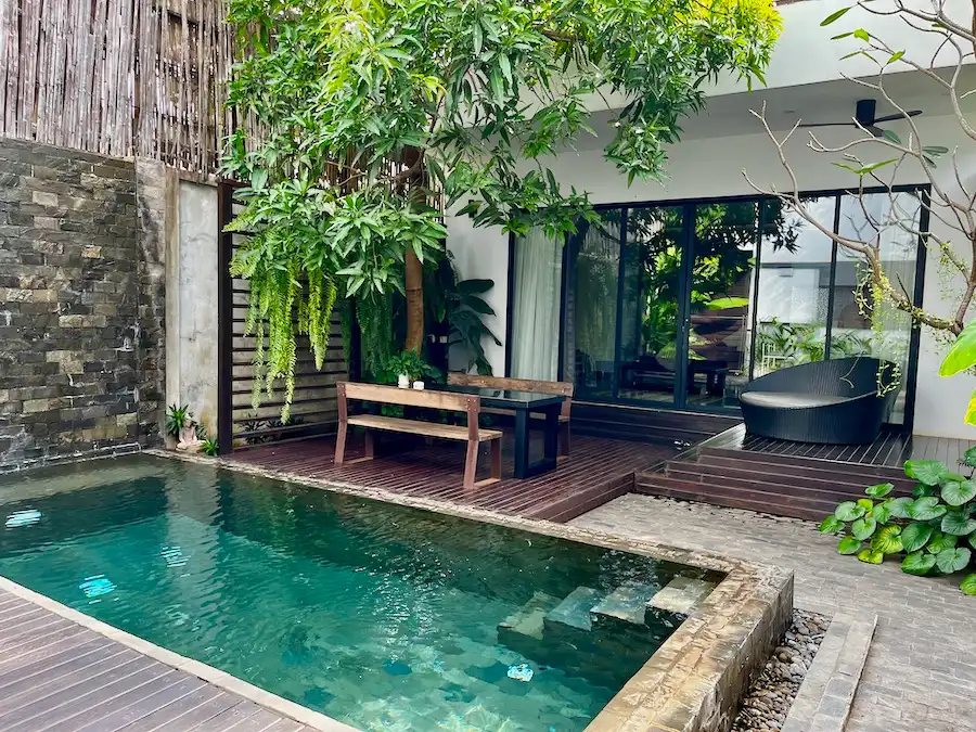 A private pool in a backyard with a tree, bench and outdoor lounge chair.
