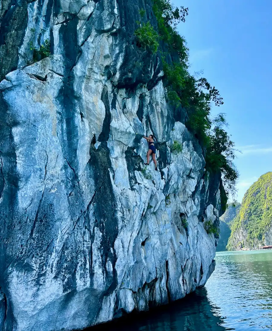 The blog author climbing up the side of a limestone rock over water.