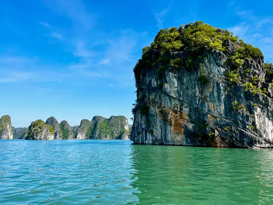 A giant limestone rock with trees coming out of emerald-green water.