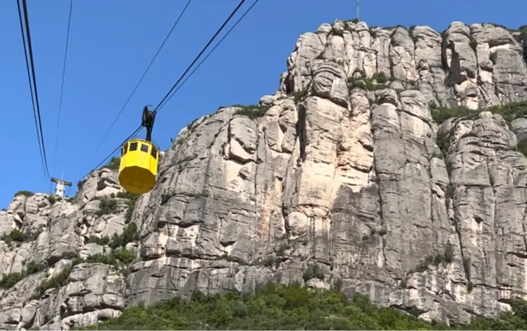 A yellow cable car passing by stone mountains.