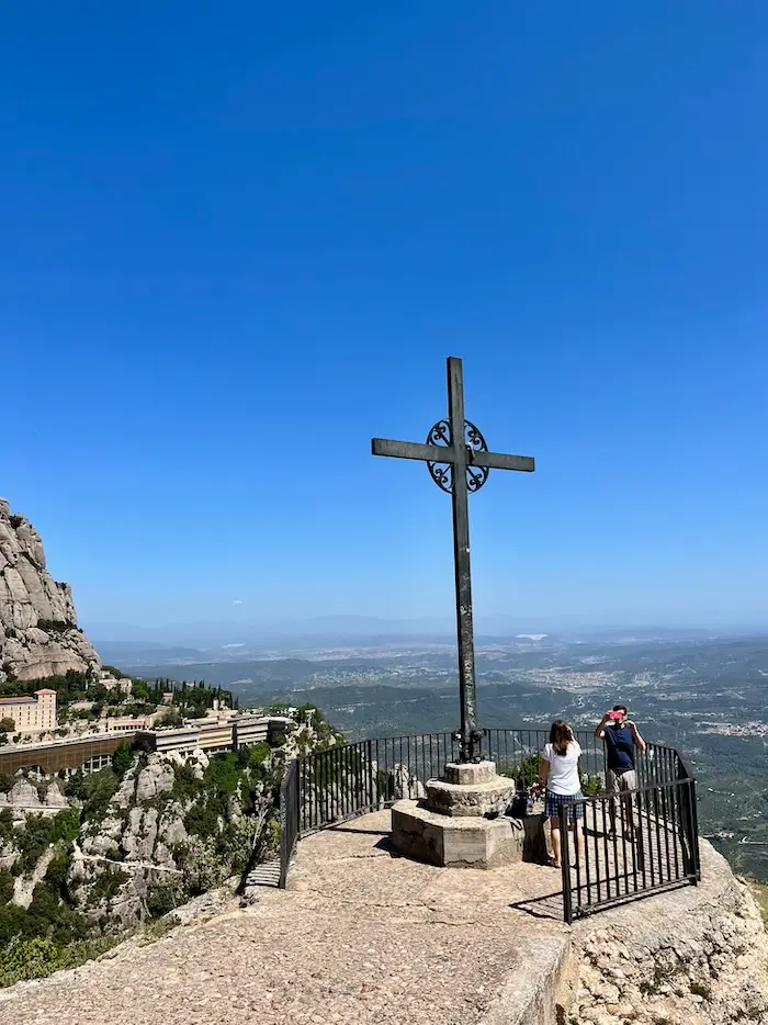 A cross structure near the edge of a mountain with a valley backdrop.