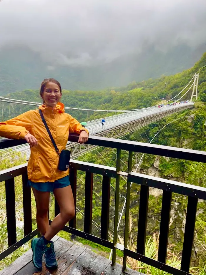 The blog author posing in front of a suspension bridge on a rainy day.