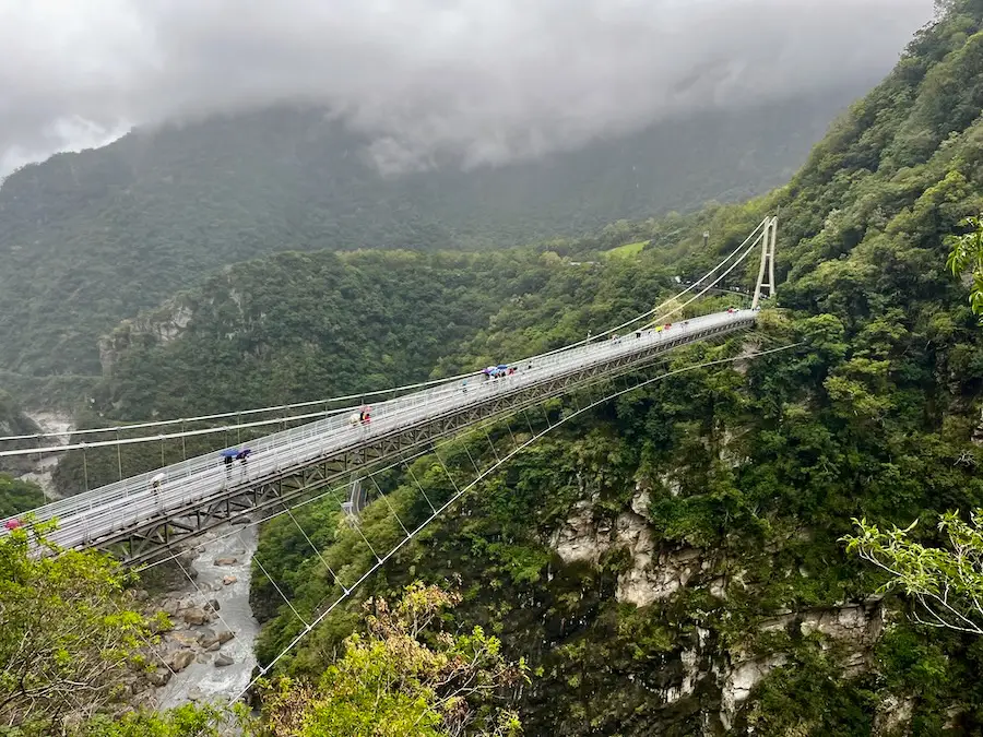A suspension bridge that reaches across a lush green mountain.