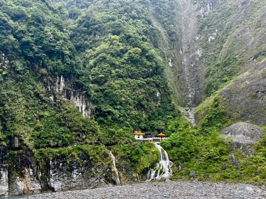 A colorful shrine nested in a marble mountain with lots of green trees.