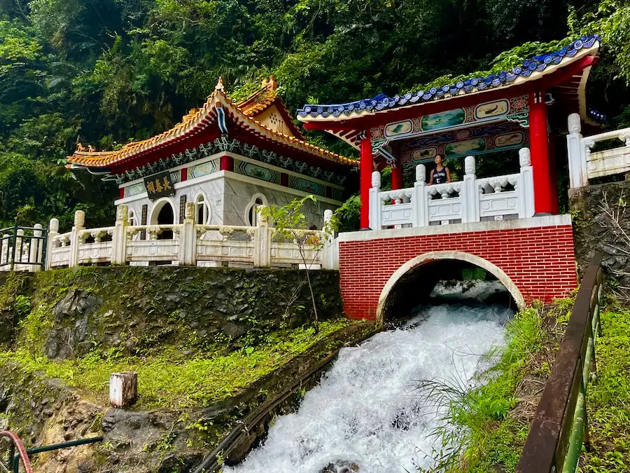 A colorful shrine with waterfall running underneath it, through an arch.