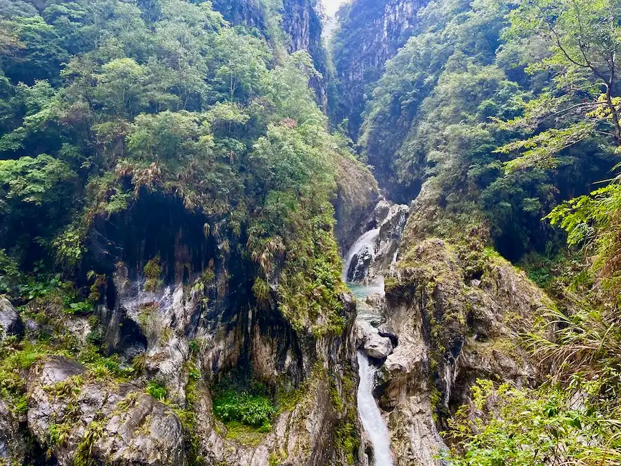 Marbled mountains with trees and a small waterfall flowing in the middle.