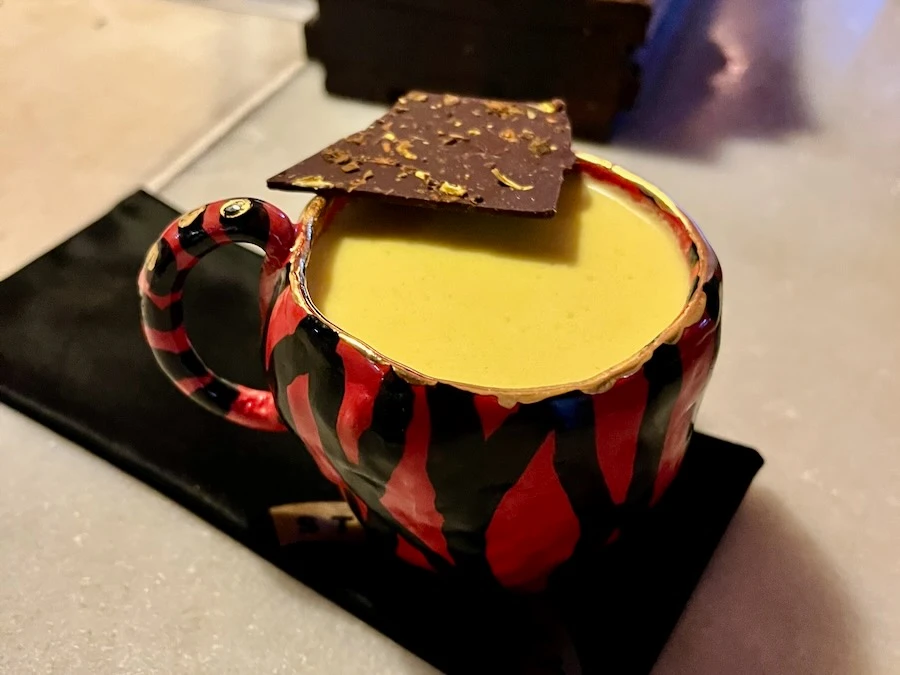 A red with black stripe cup holding a yellow liquid with a chocolate decoration at the top.