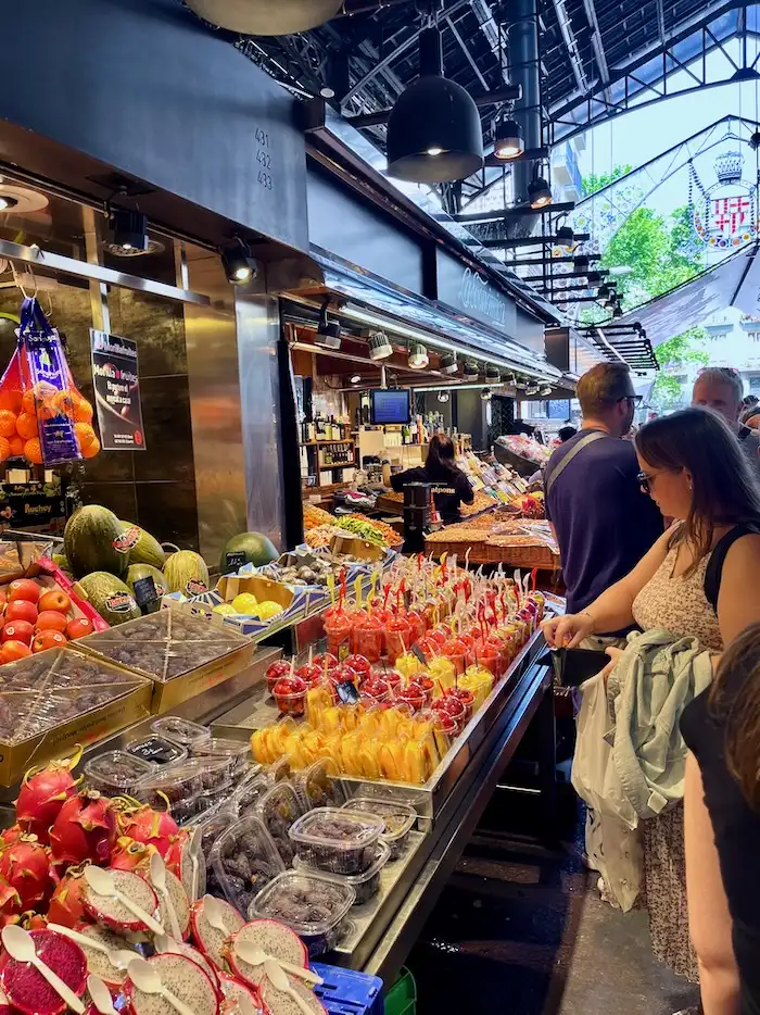 An open-air market where a vendor is selling watermelon and other fruits.