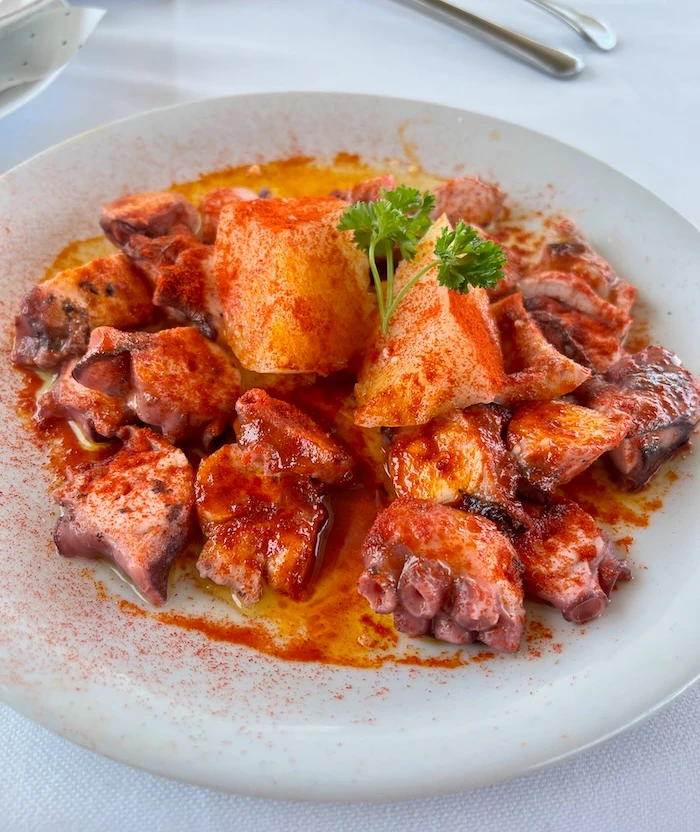 A plate of octopus and potato covered in red paprika.