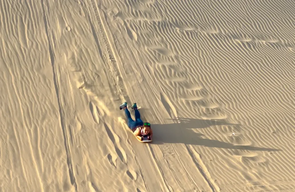 A woman on a board sliding down a sand dune.