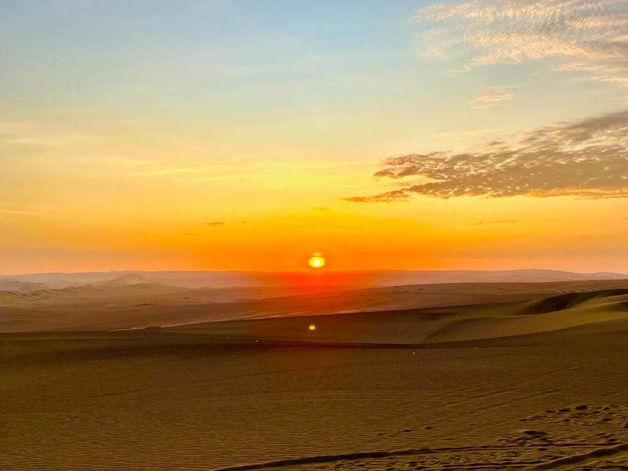A sun setting over a vast desert with sand dunes.
