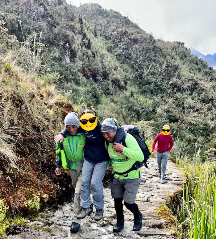 Two men carrying a woman around their shoulders on a mountain trail.