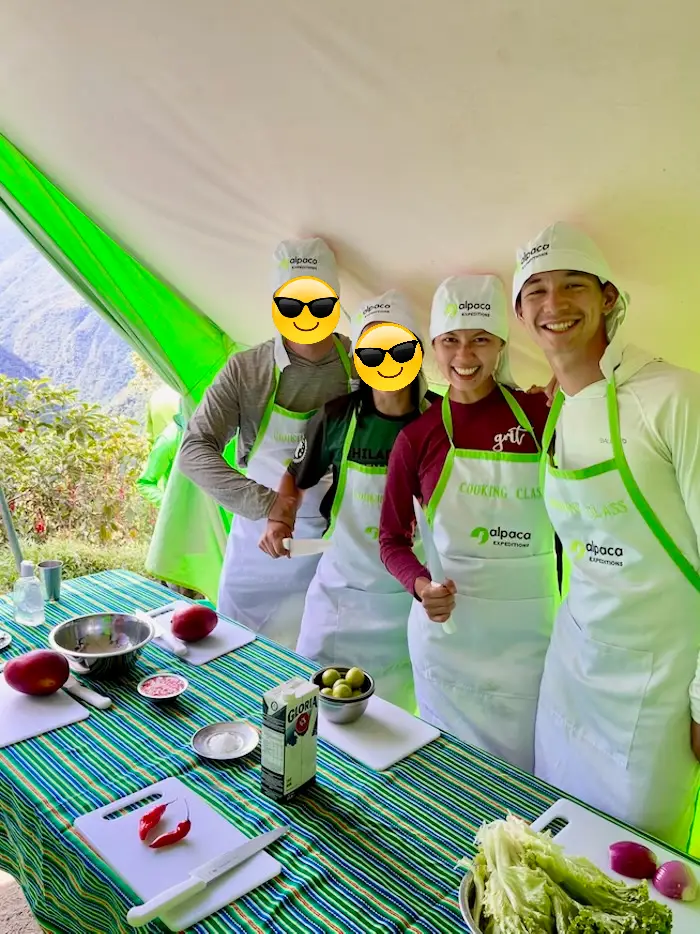 Four people wearing an apron and chef hat under a tent about to chop and cook.