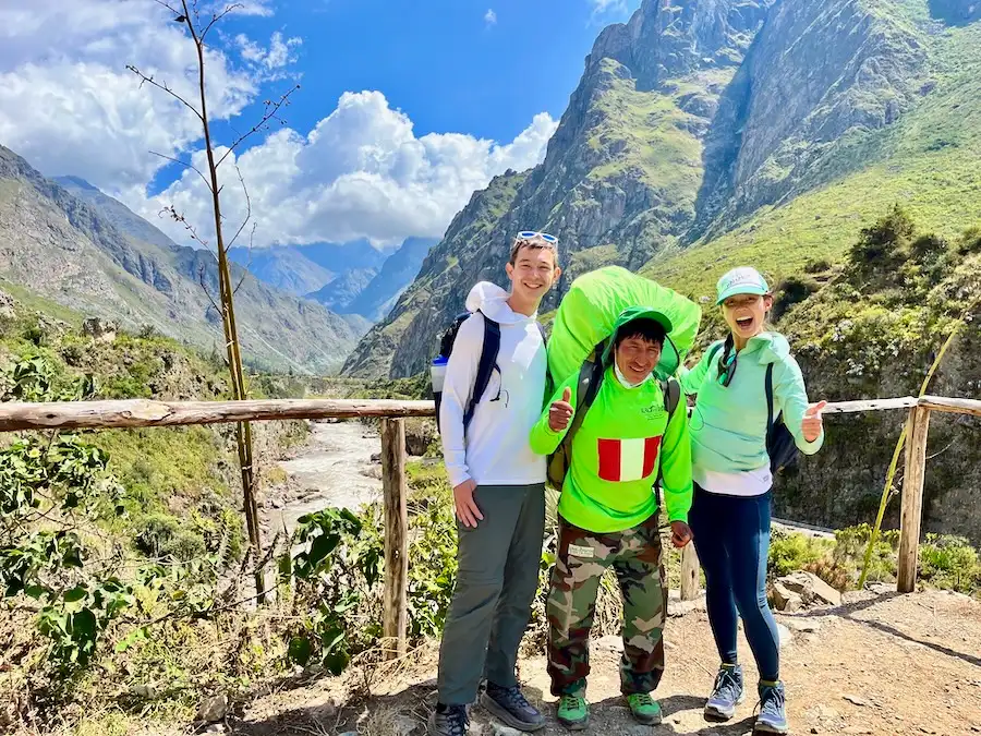 Two tourists on a mountain and a porter carrying a large bag is between them.